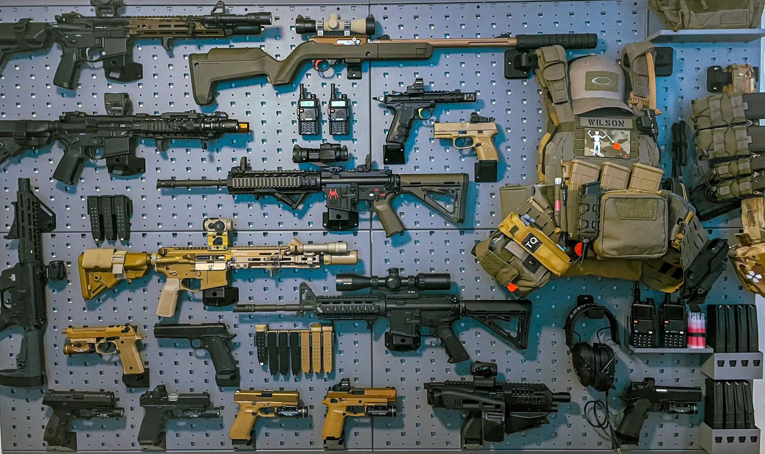 Collection of various firearms and tactical gear on a pegboard wall.